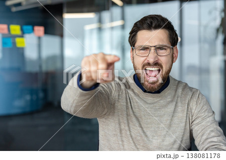 Angry man in glasses shouting loudly and pointing his finger forward, expressing strong frustration, aggression, conflict, and blame in a modern office environment Angry man in glasses shouting loudly and pointing his finger forward, expressing strong frustration, aggression, conflict, and blame in a modern office environment 138081178