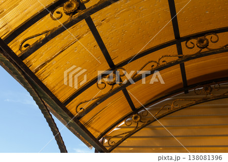 Outdoor shelter roof with transparent panels and metal frame structure, weathered surface with dirt stains against sky Outdoor shelter roof with transparent panels and metal frame structure, weathered surface with dirt stains against sky 138081396