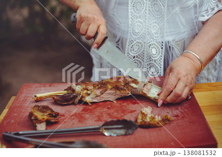 A close-up horizontal shot of a person's hands using a knife to carve a succulent roasted leg of lamb on a red professional cutting board. A close-up horizontal shot of a person's hands using a knife to carve a succulent roasted leg of lamb on a red professional cutting board. 138081532