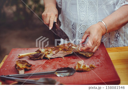 A close-up horizontal shot of a person's hands using a knife to carve a succulent roasted leg of lamb on a red professional cutting board. A close-up horizontal shot of a person's hands using a knife to carve a succulent roasted leg of lamb on a red professional cutting board. 138081546