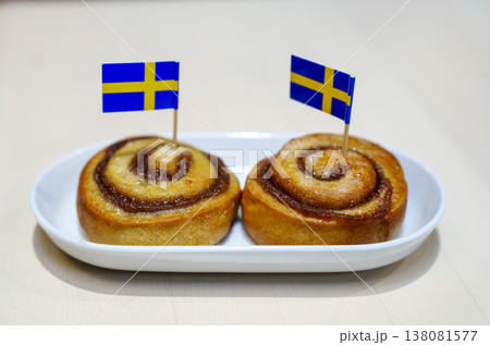 Two traditional Swedish cinnamon rolls, known as kanelbullar, served on a white ceramic plate. Each pastry is decorated with a small Swedish flag. Perfect for fika or Swedish culture concepts. 138081577