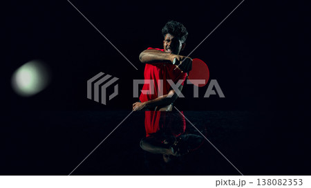 Table tennis player hitting ball with powerful stroke in dark studio. 138082353