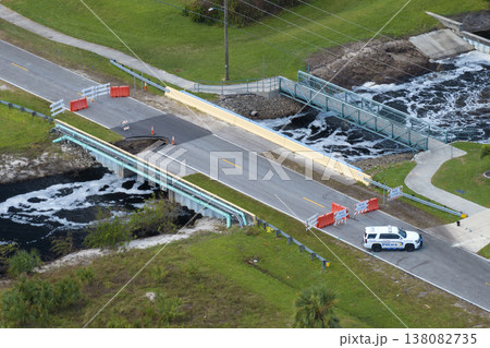 Police car blocking road access at destroyed bridge after hurricane flooding in Florida. Law enforcement patrolling at roadwork site. Reconstruction of damaged road after flood water washed asphalt 138082735