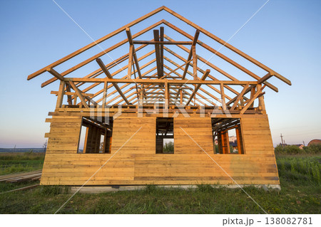 New cottage of natural ecological lumber materials under construction in green field. Wooden walls and steep roof frame. Property, investment, professional building and reconstruction concept. New cottage of natural ecological lumber materials under construction in green field. Wooden walls and steep roof frame. Property, investment, professional building and reconstruction concept. 138082781