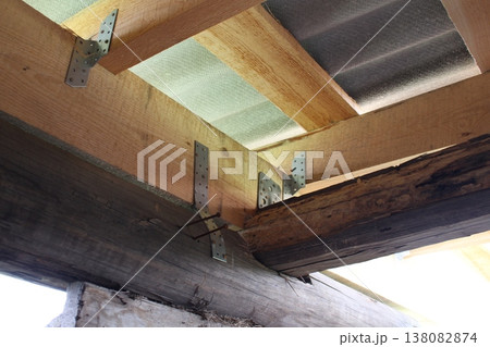 Close-up of wooden roof structure with steel angle brackets fastening beams, corrugated sheets installed above Close-up of wooden roof structure with steel angle brackets fastening beams, corrugated sheets installed above 138082874
