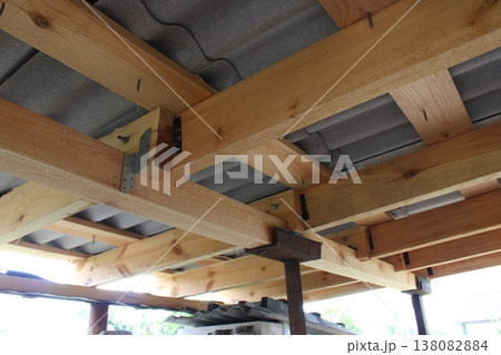 Underside view of timber roof structure with perforated metal connectors and gray corrugated roofing material above Underside view of timber roof structure with perforated metal connectors and gray corrugated roofing material above 138082884