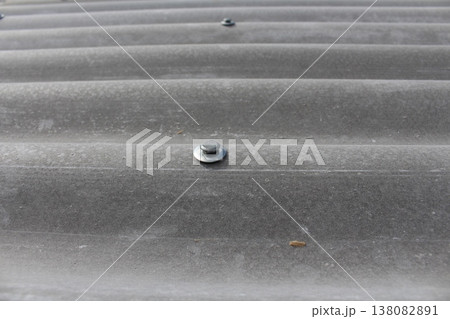 Close-up of wavy gray slate roofing panels secured with screws, showing texture and overlapping installation pattern Close-up of wavy gray slate roofing panels secured with screws, showing texture and overlapping installation pattern 138082891