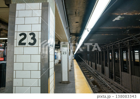 A white tiled column marked 23 stands beside underground subway tracks in Manhattan, New York City. Fluorescent lights and steel framework define the NYC metro transportation system. A white tiled column marked 23 stands beside underground subway tracks in Manhattan, New York City. Fluorescent lights and steel framework define the NYC metro transportation system. 138083343