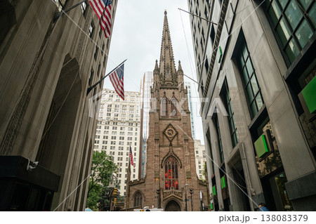 A Gothic cathedral stands between tall skyscrapers in downtown Manhattan New York. American flags and stained glass windows add historic character to the modern urban cityscape. 138083379