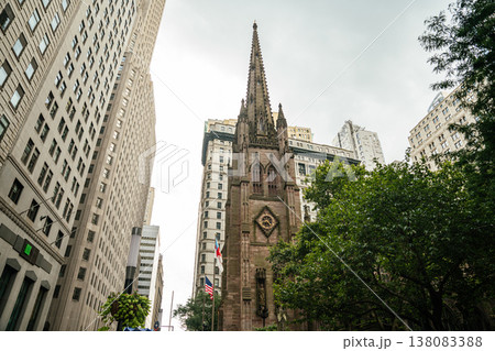 A historic Gothic church stands between tall skyscrapers in Manhattan New York. The stone facade and spire contrast with surrounding modern office buildings in the busy urban city center. A historic Gothic church stands between tall skyscrapers in Manhattan New York. The stone facade and spire contrast with surrounding modern office buildings in the busy urban city center. 138083388