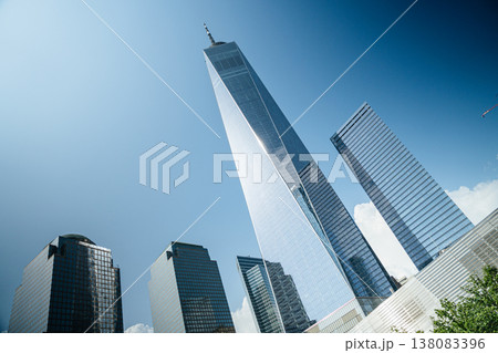 Angled perspective of One World Trade Center towering over surrounding skyscrapers in Manhattan. The modern glass facade reflects sunlight against a bright blue sky. Angled perspective of One World Trade Center towering over surrounding skyscrapers in Manhattan. The modern glass facade reflects sunlight against a bright blue sky. 138083396