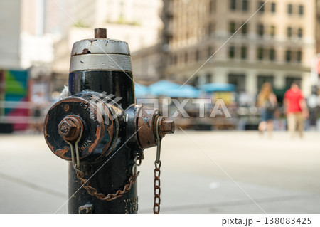 A black metal fire hydrant stands on a city sidewalk in New York with blurred pedestrians and buildings in the background. The urban street scene highlights public safety infrastructure in a busy A black metal fire hydrant stands on a city sidewalk in New York with blurred pedestrians and buildings in the background. The urban street scene highlights public safety infrastructure in a busy 138083425