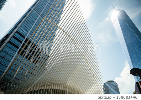 One World Trade Center rises high above the skyline of New York City next to the Oculus structure. The glass skyscraper reflects sunlight against a clear blue sky in Lower Manhattan. 138083446