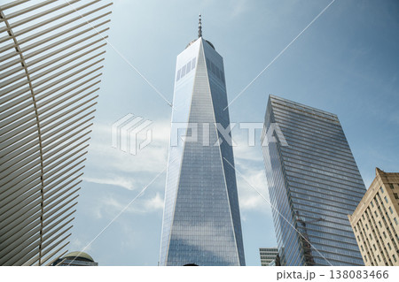 One World Trade Center towers into the blue sky in Lower Manhattan, New York City. The modern glass skyscraper reflects clouds above the downtown financial district. One World Trade Center towers into the blue sky in Lower Manhattan, New York City. The modern glass skyscraper reflects clouds above the downtown financial district. 138083466