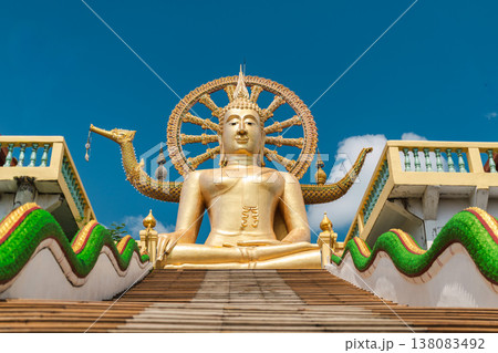 Majestic golden Buddha statue at Thai temple with long staircase and decorative serpents under blue sky 138083492