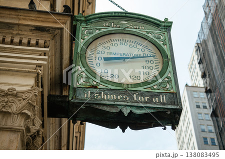 Ornate vintage thermometer sign mounted on a historic downtown building surrounded by tall city skyscrapers. The large temperature display highlights urban weather conditions in a busy metropolitan Ornate vintage thermometer sign mounted on a historic downtown building surrounded by tall city skyscrapers. The large temperature display highlights urban weather conditions in a busy metropolitan 138083495