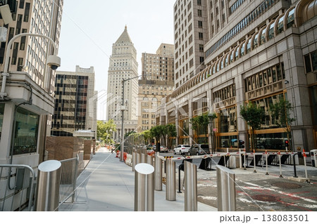 A quiet Manhattan street features a security booth and metal barriers between tall office buildings in New York City. Modern architecture and controlled access infrastructure define the downtown A quiet Manhattan street features a security booth and metal barriers between tall office buildings in New York City. Modern architecture and controlled access infrastructure define the downtown 138083501