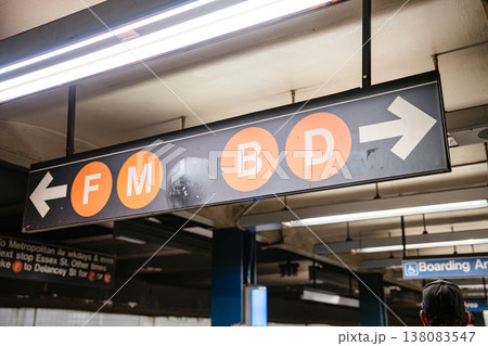 Overhead subway direction sign showing F M B and D train lines at Broadway Lafayette Street station in New York City. Underground metro scene with fluorescent lighting and urban transit infrastructure Overhead subway direction sign showing F M B and D train lines at Broadway Lafayette Street station in New York City. Underground metro scene with fluorescent lighting and urban transit infrastructure 138083547