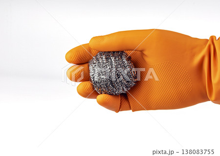 Hand Wearing Orange Rubber Latex Protective Glove Holding a Shiny Metallic Steel Wool Scrubber Ball for Kitchen Cleaning and Dishwashing Tasks on White Background Hand Wearing Orange Rubber Latex Protective Glove Holding a Shiny Metallic Steel Wool Scrubber Ball for Kitchen Cleaning and Dishwashing Tasks on White Background 138083755