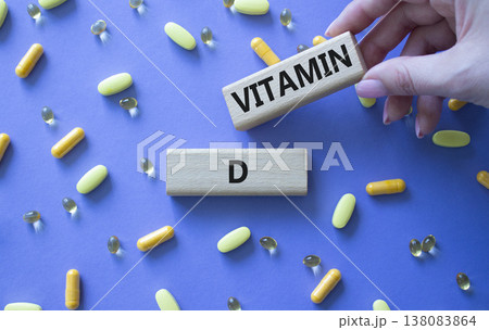 Vitamin D symbol. Concept word Vitamin D on wooden blocks. Beautiful purple background with pills. Doctor hand. Medicine and Vitamin D concept. Copy space Vitamin D symbol. Concept word Vitamin D on wooden blocks. Beautiful purple background with pills. Doctor hand. Medicine and Vitamin D concept. Copy space 138083864