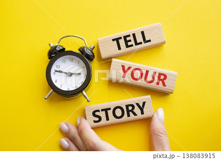 Tell your story symbol. Wooden blocks with words Tell your story. Businessman hand. Beautiful yellow background with alarm clock. Business and Tell your story concept. Copy space. 138083915