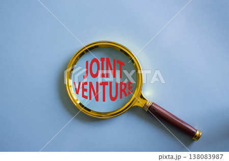 Joint Venture symbol. Magnifying Glass with words Joint Venture. Beautiful blue background. Business and Joint Venture concept. Copy space. 138083987
