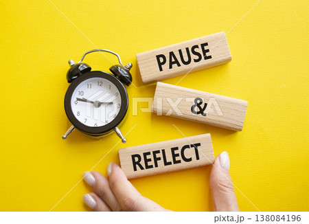 Pause and Reflect symbol. Concept words Pause and Reflect on wooden blocks. Businessman hand. Beautiful yellow background with alarm clock. Business and Pause and Reflect concept. Copy space. Pause and Reflect symbol. Concept words Pause and Reflect on wooden blocks. Businessman hand. Beautiful yellow background with alarm clock. Business and Pause and Reflect concept. Copy space. 138084196