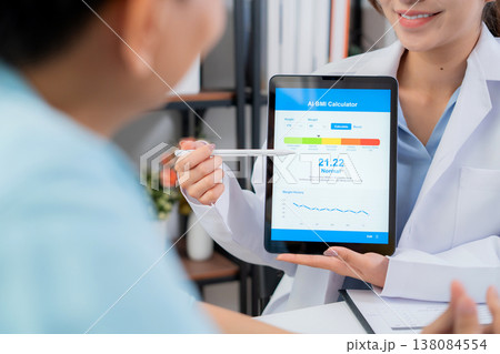 Asian woman nutritionist showing AI BMI calculator on tablet and explaining to man patient. Asian woman nutritionist showing AI BMI calculator on tablet and explaining to man patient. 138084554