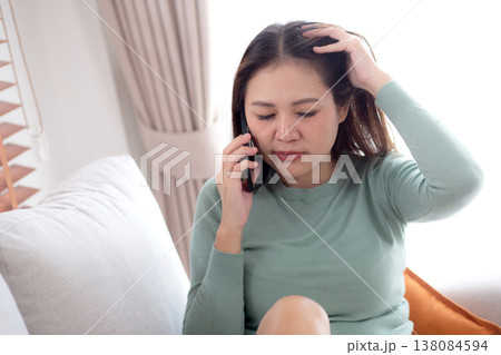 Asian young woman stress and worried sitting on sofa while speaking on smart phone in living room. Asian young woman stress and worried sitting on sofa while speaking on smart phone in living room. 138084594
