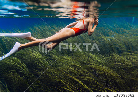 Woman swims underwater over algae at the bottom in freshwater lake. Freediving in crystal lake 138085662