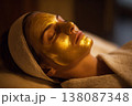 elegant woman relaxing during gold facial therapy session in upscale spa, serene mood, warm ambient 138087348