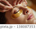 beautician applying gold eye patches to female client during facial treatment, elegant spa 138087353