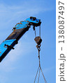 A photograph of the top of an old construction crane with peeling blue paint and rust. The boom hook lifts a load on twisted metal cables. The vertical shot is against a cloudless blue sky 138087497