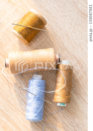Colorful thread spools and sewing needles lying on a wooden surface, representing craft, hobby, and textile work 138087881