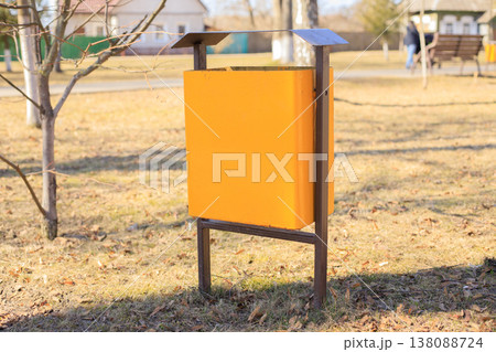 Yellow metal trash can in a public city park. Modern municipal waste container Yellow metal trash can in a public city park. Modern municipal waste container 138088724