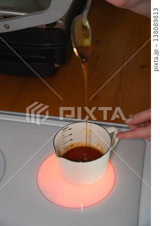 Hands stir honey in measuring cup on heated stovetop during baking preparation in home kitchen. Cooking process, ingredient preparation, homemade pastry, lifestyle content, kitchen Hands stir honey in measuring cup on heated stovetop during baking preparation in home kitchen. Cooking process, ingredient preparation, homemade pastry, lifestyle content, kitchen 138089813