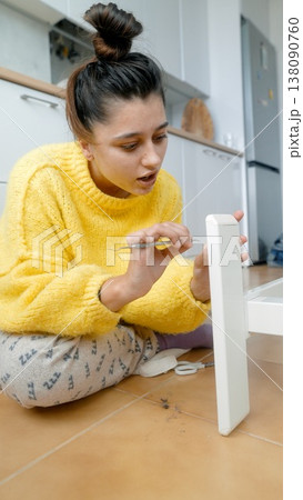 Female Individual Sitting On Floor Using Screwdriver To Secure Brackets On White Wallmounted Shelving 138090760