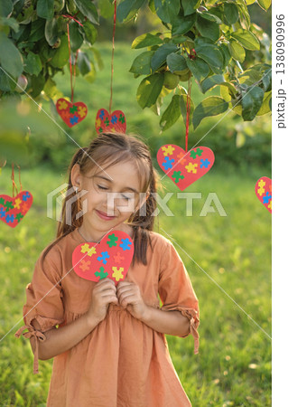 A gentle, sensual girl lovingly holds a heart-shaped postcard decorated with puzzles for autism Day 138090996