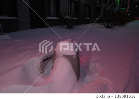 Street infrastructure buried in deep snow near residential buildings during winter evening snowfall. The dark urban landscape reflects harsh weather, seasonal climate and winter conditions in the city 138091618