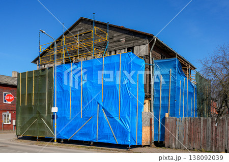 Old wooden house under renovation with scaffolding and blue protective cover on urban street Old wooden house under renovation with scaffolding and blue protective cover on urban street 138092039