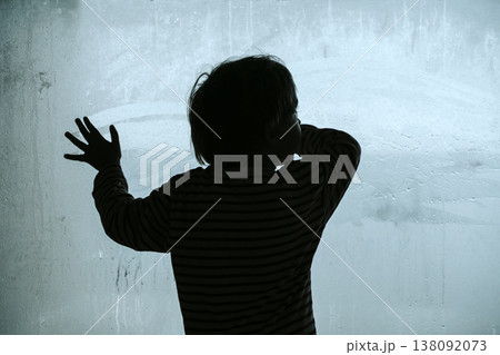 Silhouette of a lonely child looking through a large cold fogged window. A conceptual photography work exploring themes of childhood depression, psychological crisis, and the deep feeling of isolation 138092073