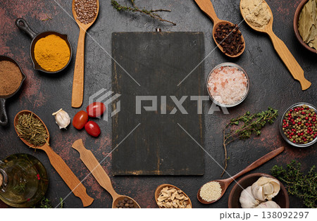 A cutting board is surrounded by spices turmeric, cloves, pepper, salt, sesame seeds, flax, and ginger A cutting board is surrounded by spices turmeric, cloves, pepper, salt, sesame seeds, flax, and ginger 138092297