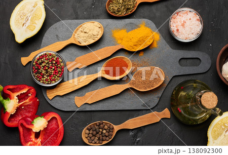 Wooden spoons with ground spices on a black board surrounded by red pepper halves, lemon, bowls with salt and peppercorns Wooden spoons with ground spices on a black board surrounded by red pepper halves, lemon, bowls with salt and peppercorns 138092300