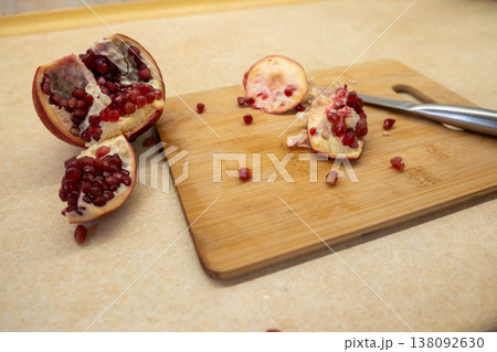 Cut pomegranate on cutting board with scattered arils 138092630
