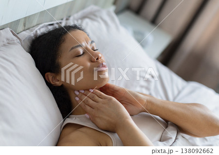 Young black woman lying in bed touching neck with discomfort 138092662