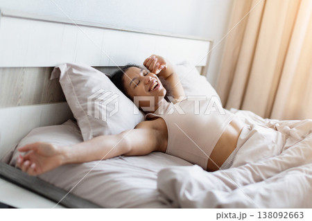 Young black woman lying in bed smiling and stretching after waking up 138092663
