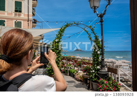 Woman capturing views of gallinara island from a lively beachside area in alassio, liguria, using a smartphone, showing tourism and technology integration Woman capturing views of gallinara island from a lively beachside area in alassio, liguria, using a smartphone, showing tourism and technology integration 138093928