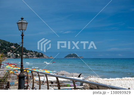 Alassio beach in the ligurian riviera, showing colorful umbrellas, the tranquil sea, a classic street lamp, and gallinara island under a clear blue sky Alassio beach in the ligurian riviera, showing colorful umbrellas, the tranquil sea, a classic street lamp, and gallinara island under a clear blue sky 138093929
