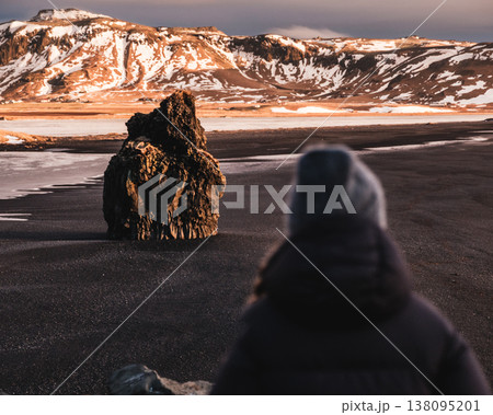 Woman viewing Arnardrangur sea stack on Reynisfjara black sand beach, South Iceland. Woman viewing Arnardrangur sea stack on Reynisfjara black sand beach, South Iceland. 138095201