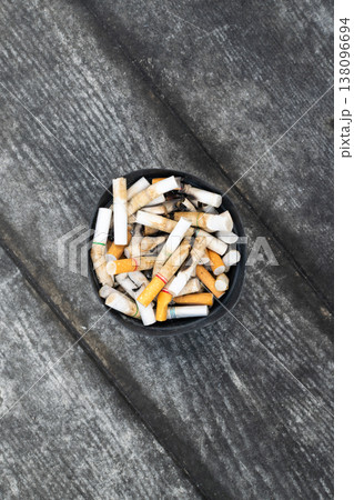 Top view of used cigarette butts in ashtray on rough surface highlighting smoking habit addiction pollution waste and unhealthy lifestyle with copy space Top view of used cigarette butts in ashtray on rough surface highlighting smoking habit addiction pollution waste and unhealthy lifestyle with copy space 138096694